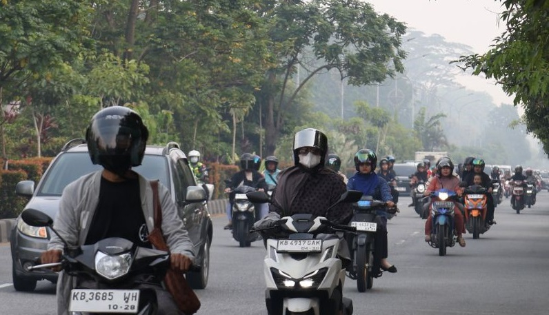 Sejumlah pengendara motor melintasi jalan yang diselimuti kabut asap